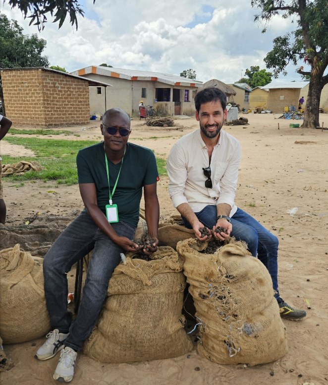 Two Ivoire Essentials team members sitting on sacks and holding shea nuts during field purchasing in Côte d’Ivoire